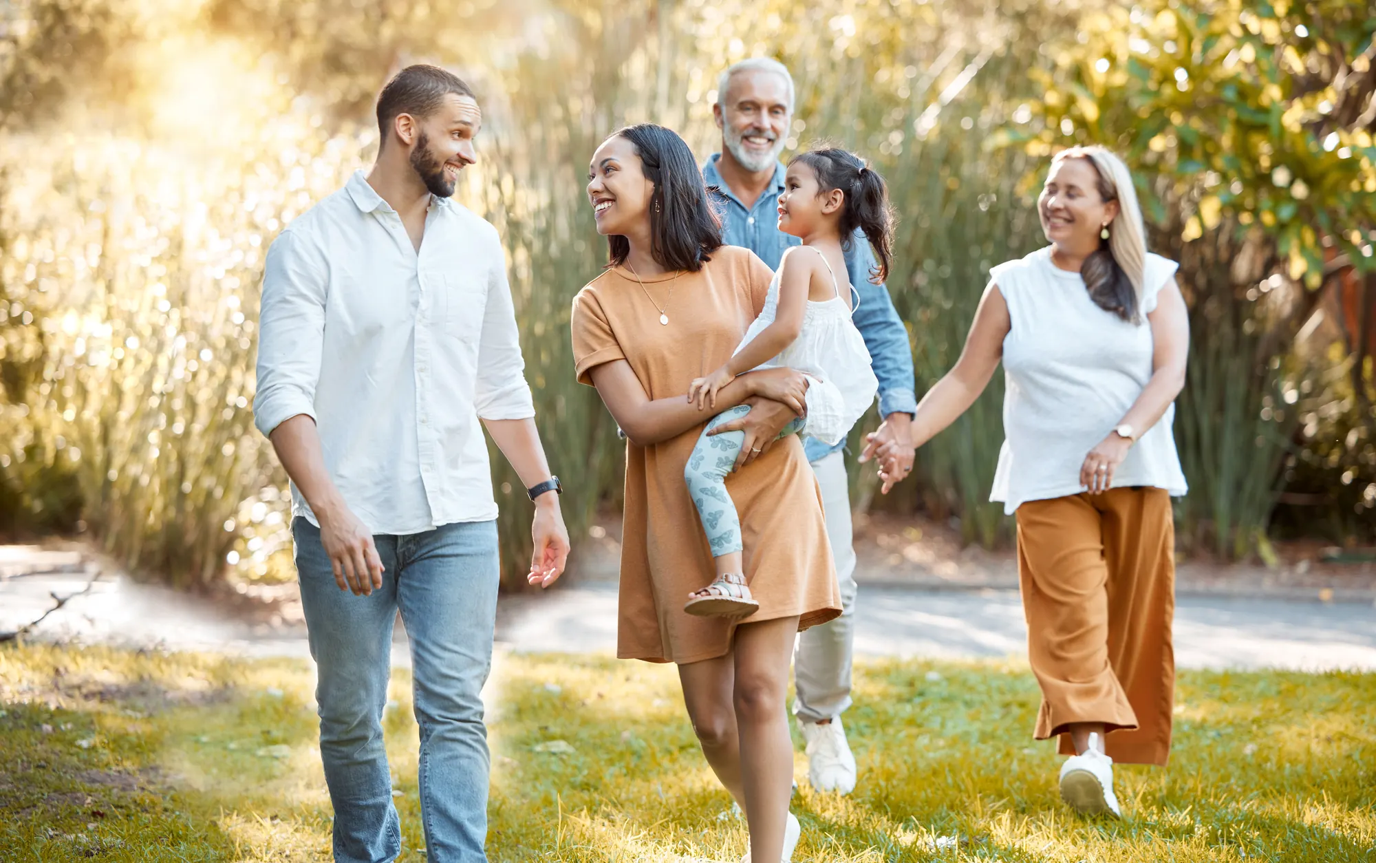 Three generations of a family walking together through a sunlit garden