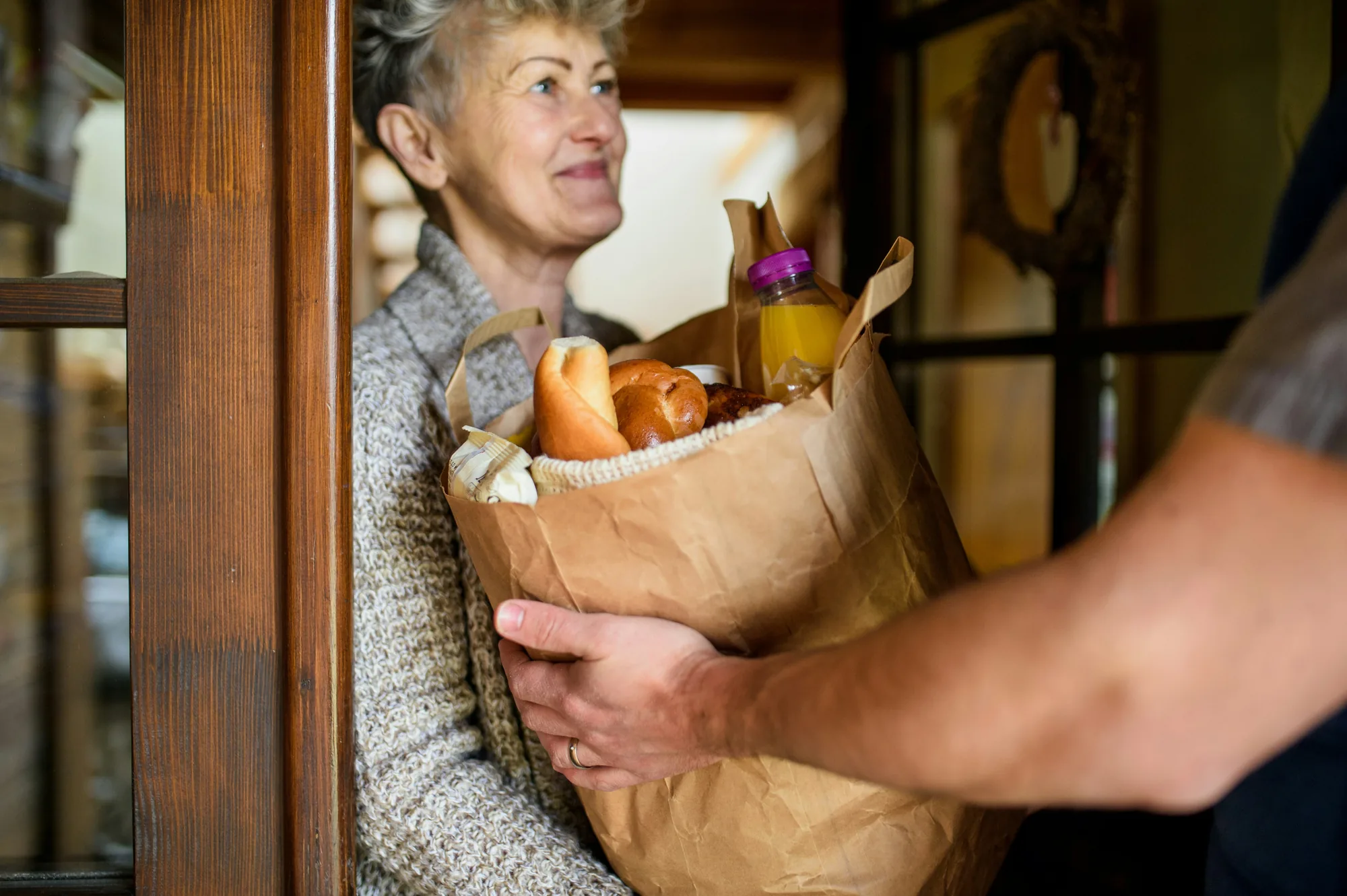 A Here 2 Helper delivering a bag of groceries to a customer at her front door